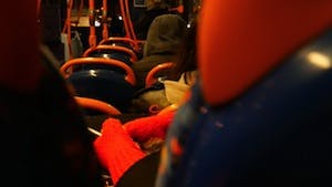 Inside the D bus at night a girl wears orange gloves