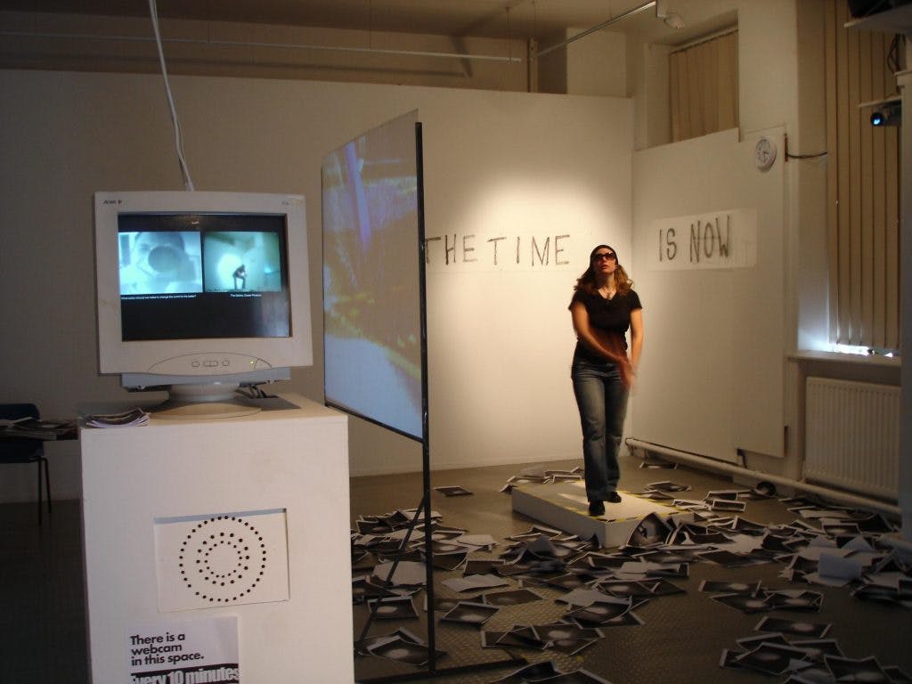 Cat in a gallery with a computer and lots of black and white computer print outs on the floor